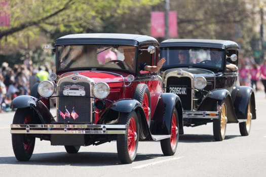 Washington, D.C., USA - April 14, 2018 Classic cars with american flags going down the street in the 2018 National Cherry Blossom Parade