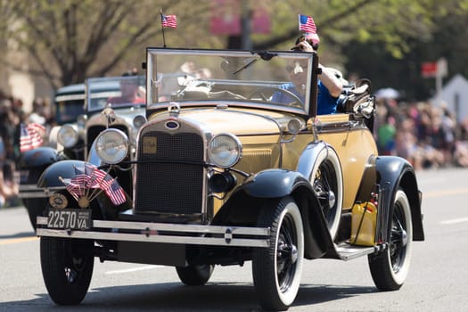 Washington, D.C., USA - April 14, 2018 Classic cars with american flags going down the street in the 2018 National Cherry Blossom Parade