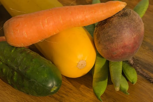 Carrot, cucumber, bean, zucchini, and red beet sitting on a table in warm light.