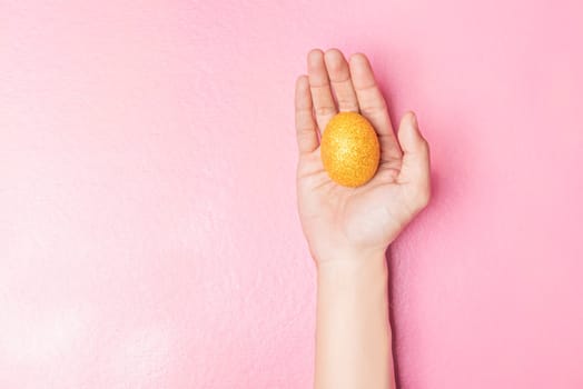 Human hand holding yellow easter egg on pink color background. Happy Easter