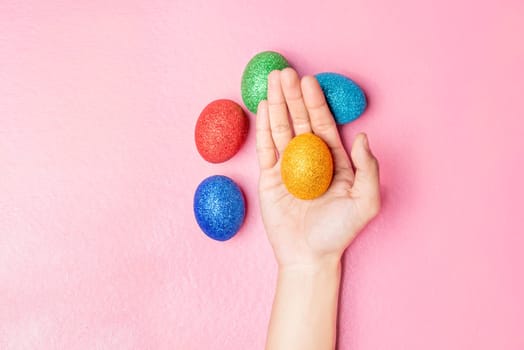 Human hand holding yellow easter egg and colorful easter eggs on pink color background. Happy Easter