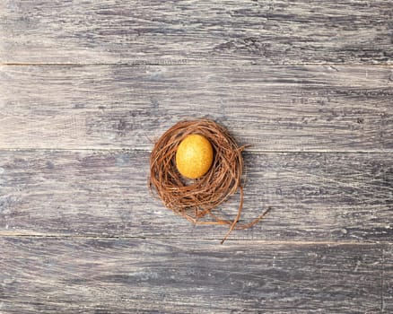 Yellow easter egg in the nest on wooden table. Happy Easter