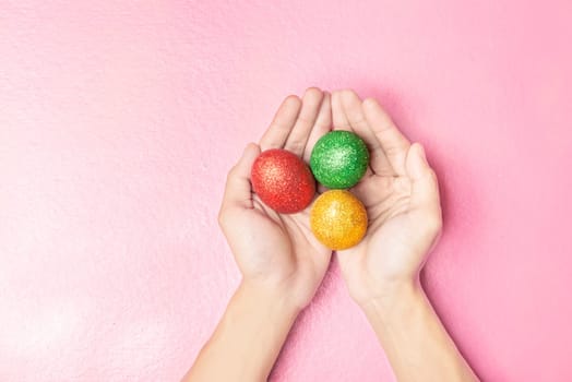 Human hands holding colorful easter eggs over pink color background. Happy Easter