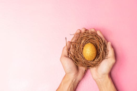 Human hands holding the nest with easter eggs over pink color background. Happy Easter