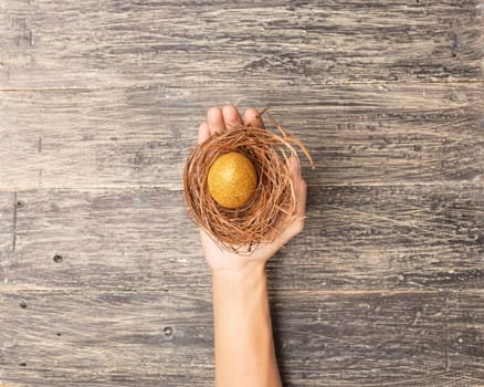 Human hand holding the nest with easter eggs over wooden table background. Happy Easter