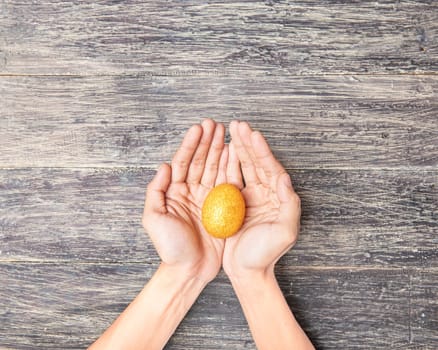 Human hands holding yellow easter egg over wooden table background. Happy Easter