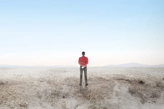 Rear view of asian businessman standing on the dry land over blue sky background. Earth day concept