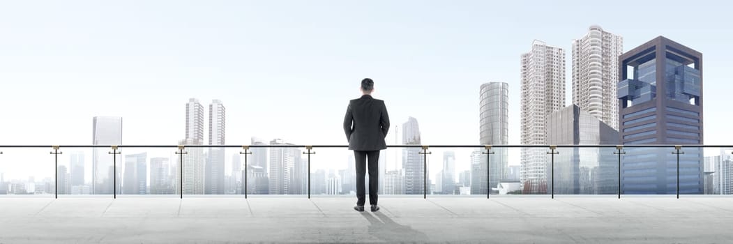 Rear view of asian businessman standing on modern terrace and looking at view on the city
