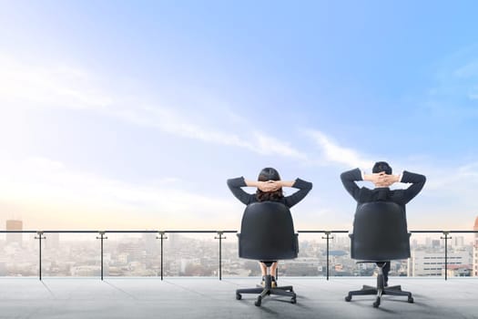 Rear view of two asian business people sitting on the office chair in modern terrace relax and looking at view on the city over blue sky background