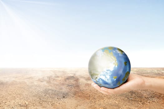 Human hand holding earth planet with dry land over blue sky background. Earth day concept