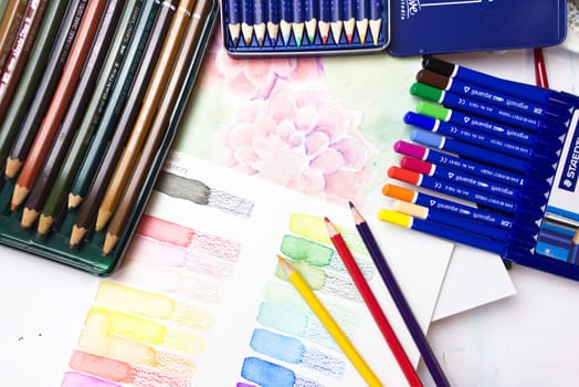 different watercolor pencil brands on a desk with some in-progress illustrations