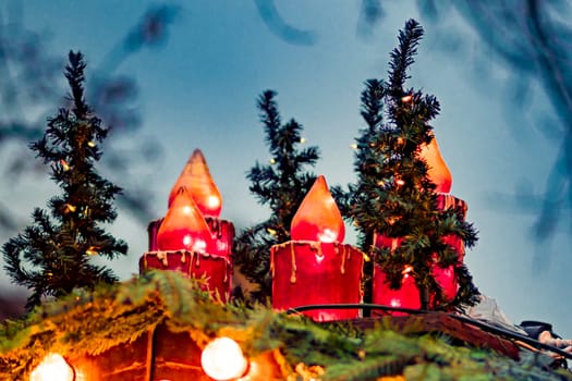 Big red plastic christmas candles are standing on a hut roof with fir branches and blue background