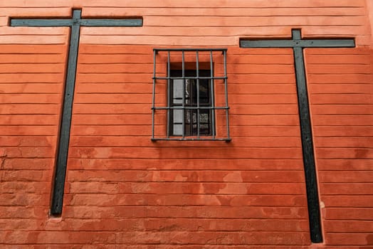 Two crosses on a red wall with a barred window in Seville, Spain
