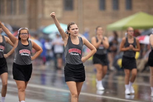 Peru, Indiana, USA - July 21, 2018 Under heavy rain cheerleader waring shirts that say Warrior Cheerleader dance at the Circus City Festival Parade