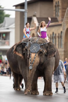 Peru, Indiana, USA - July 21, 2018 Young women riding elephants down the road at the Circus City Festival Parade