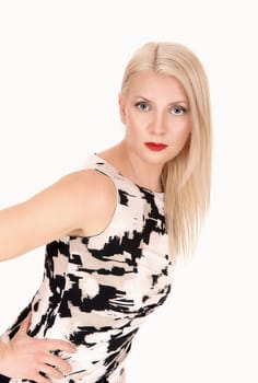 A gorgeous middle age woman in a light color dress with long blond.hair standing, looking into the camera, isolated for white background.