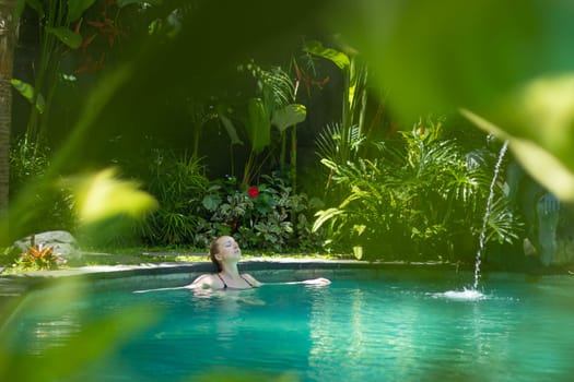 Sensual young woman relaxing in outdoor spa infinity swimming pool surrounded with lush tropical greenery of Ubud, Bali. Wellness, natural beauty and body care concept.