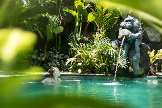Sensual young woman relaxing in outdoor spa infinity swimming pool surrounded with lush tropical greenery of Ubud, Bali. Wellness, natural beauty and body care concept.