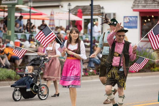 Frankenmuth, Michigan, USA - June 10, 2018 Men and women wearing traditional german clothing going down the road waving american flags at the Bavarian Festival Parade.
