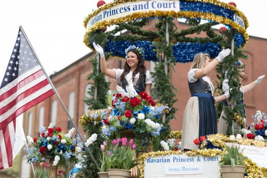 Holland, Michigan, USA - May 12, 2018 Beuty Queens on top of a float surrounded by tulip flowers and wearing traditional dutch clothing go down the road at the Muziek Parade, during the Tulip Time Festival