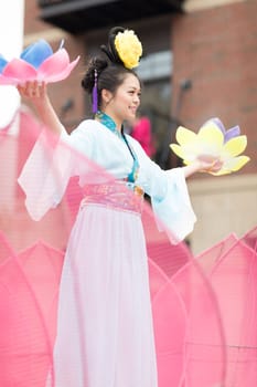 Holland, Michigan, USA - May 12, 2018 Chinese woman wearing a kimono riding on a float in the shape of tulip flowers while holding tulip flowers on her hands at the Muziek Parade, during the Tulip Time Festival
