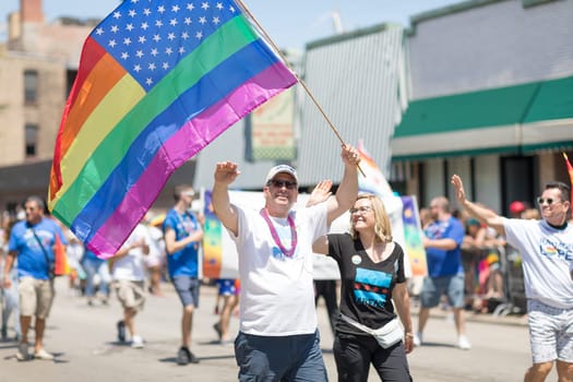 Chicago, Illinois, USA - June 24, 2018 Man waving an American Flag with the rainbow collors, waves at the camera during the LGBTQ Pride Parade in Chicago