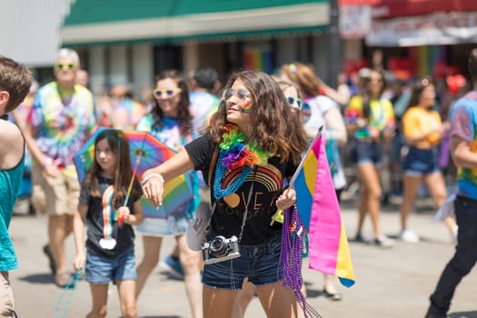 Chicago, Illinois, USA - June 24, 2018 Young woman with an old camera waving the rainbow flag, throwing beads to the spectators during the LGBTQ Pride Parade in Chicago