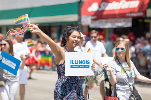 Chicago, Illinois, USA - June 24, 2018 Asian woman promoting the Illinois senate democrats, waving the rainbow flag  during the LGBTQ Pride Parade in Chicago