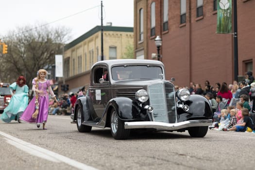 Holland, Michigan, USA - May 12, 2018 Members of Everafter West Michigan dress up as disney princess  with a classic car on the foreground, at the Muziek Parade, during the Tulip Time Festival