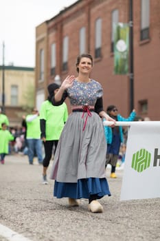 Holland, Michigan, USA - May 12, 2018 Woman wearing traditional dutch clothing waving walking down the road at the Muziek Parade, during the Tulip Time Festival