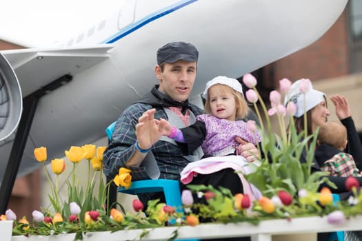 Holland, Michigan, USA - May 12, 2018 Father and daughter wearing traditional dutch clothing waving at the camera surrounded by tulip flowers at the Muziek Parade, during the Tulip Time Festival