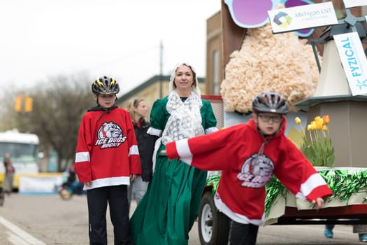 Holland, Michigan, USA - May 12, 2018 Woman wearing traditional clothing and children with Ice Dogs Hockey shirts going down the road at the Muziek Parade, during the Tulip Time Festival