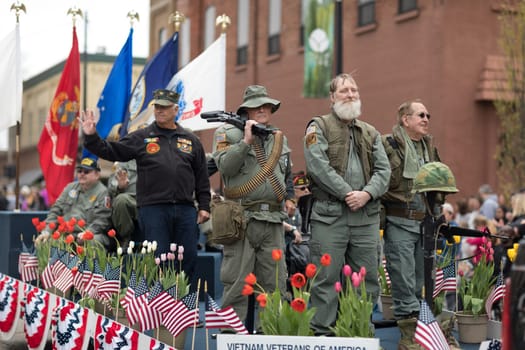 Holland, Michigan, USA - May 12, 2018 Veteran in military uniforms carry guns on top of a float, go down the road at the Muziek Parade, during the Tulip Time Festival