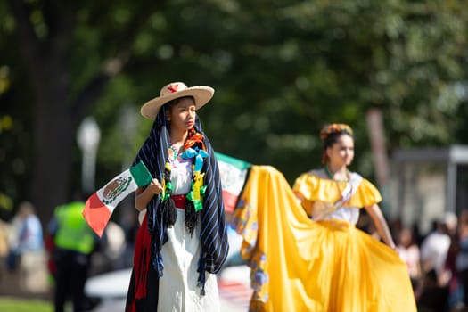 Washington, D.C., USA - September 29, 2018: The Fiesta DC Parade, woman wearing traditional clothing from Mexico going down the street carrying the mexican flag