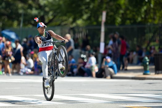 Washington, D.C., USA - September 29, 2018: The Fiesta DC Parade, Young man riding a bicycle performing a stunt, wearing a hat with the Dominican Republic Flag