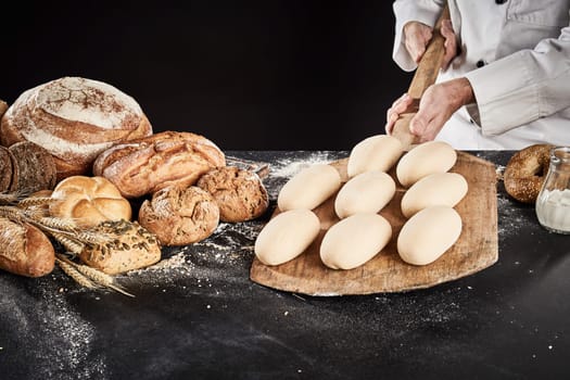 Ready to cook loaves of bread dough on a wooden paddle held by a chef over a counter with display of assorted gourmet breads