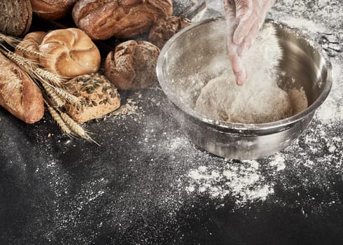 Baker dusting his dough with flour from his hands as he prepares the mixture in a bowl while making an assortment of breads on display