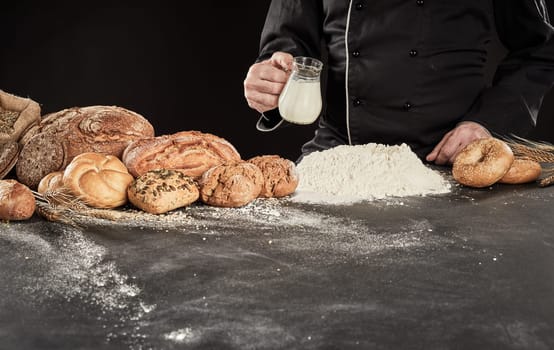 Specialist baker pouring milk into a heap of flour as he prepares the dough for his gourmet bread displayed alongside