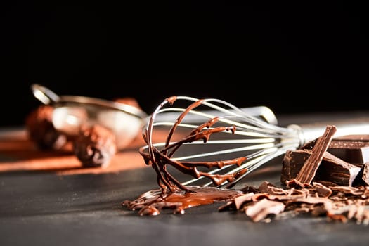 Preparing chocolate bonbons with an old whisk to beat the melted chocolate ingredient lying on a kitchen table in a low angle view