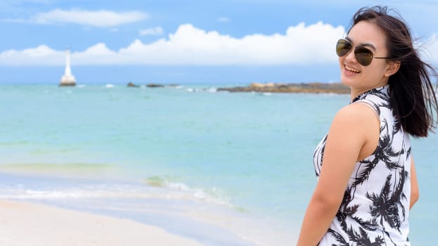 Beautiful woman tourist wearing sunglasse looking at the camera and smiling with happy on the beach and sea in summer sky background at Tarutao island, Satun, Thailand, 16:9