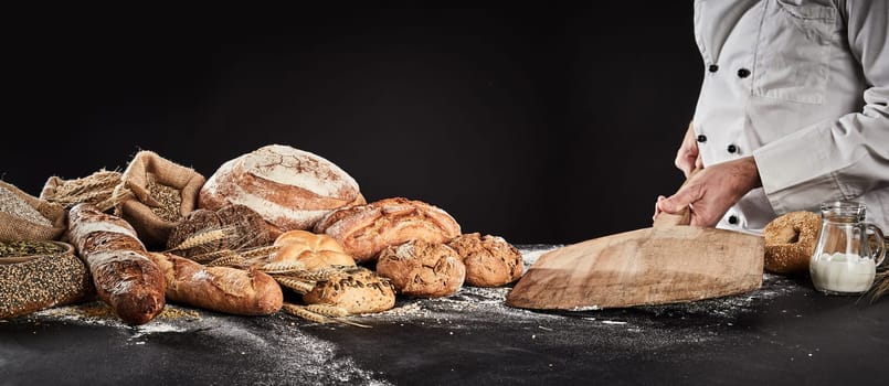 Baker placing an empty wooden paddle on a table ready fore placing dough for baking with a display of speciality bread alongside
