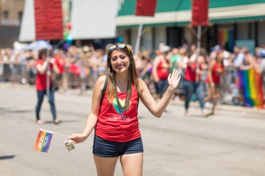 Chicago, Illinois, USA - June 24, 2018 woman waves at the camera, holding the rainbow flag and wearing a shirt that say, legal council for health justice, during the LGBTQ Pride Parade in Chicago