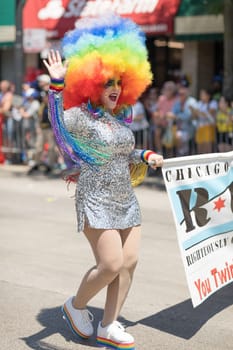 Chicago, Illinois, USA - June 24, 2018 Person with wig with the colors of the rainbow, face paint and earings in shape of hearts, waves at people during the LGBTQ Pride Parade in Chicago