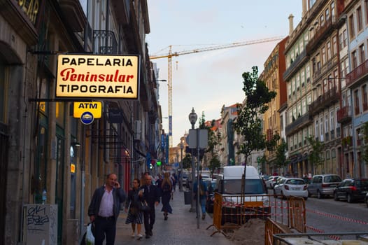 PORTO, PORTUGAL - JUNE 2, 2017: People walking by Porto Old Town street passing atm and typography, building crane in background