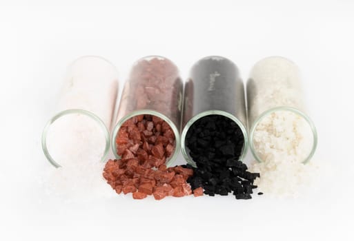 Alaea salt, hawaiian black salt, grey salt and fleur de sel pouring from jars and isolated now white.
