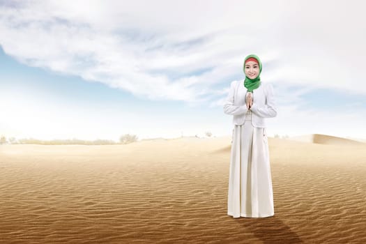 Smiling asian muslim woman in veil praying on the sand dune with blue sky background