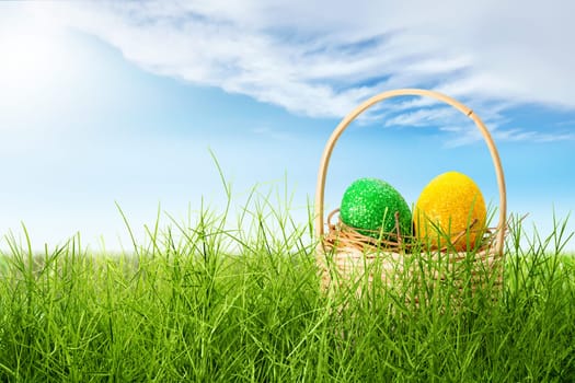 Colorful easter eggs in the nest on wooden basket on the grass field with sunlight and blue sky background. Happy Easter