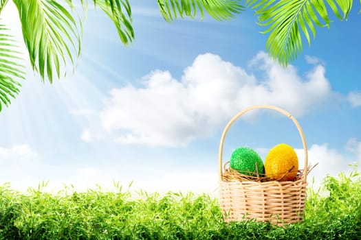 Colorful easter eggs in the nest on wooden basket on the green grass with palm branches and blue sky background. Happy Easter