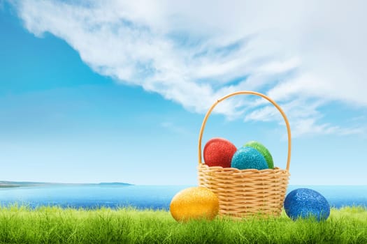 Colorful easter eggs on wooden basket and green grass with blue ocean view and cloudscapes over blue sky background. Happy Easter