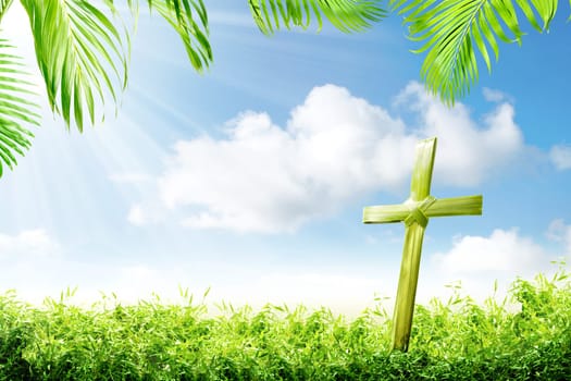 Cross shape of palm leaves on the green grass with palm branches and blue sky background. Happy Easter